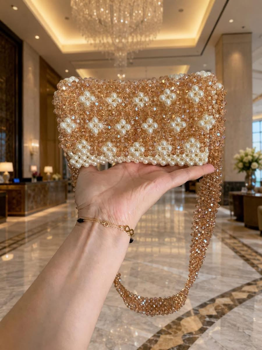 Sac de soirée Bassmera Pearl Rosé en cristaux or rose et perles blanches, tenu à la main dans un hôtel de luxe.