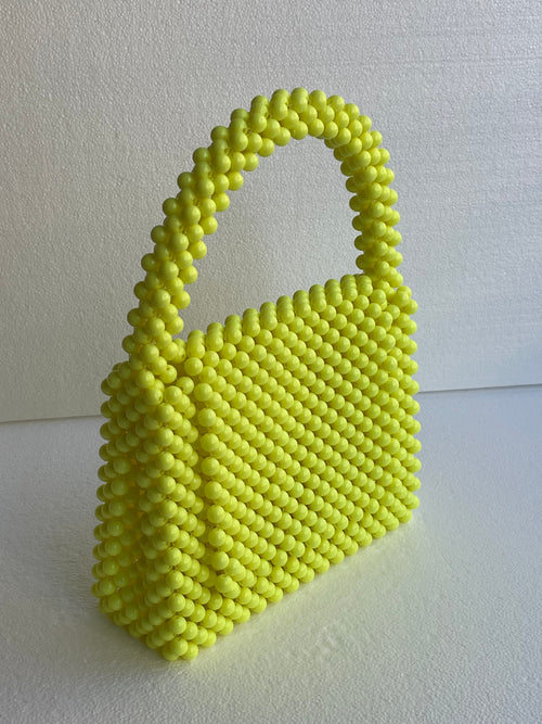 Sac à main Bassmera Citrina artisanal jaune fluo en perles, vue de face inclinée avec texture ronde uniforme et poignée arquée.