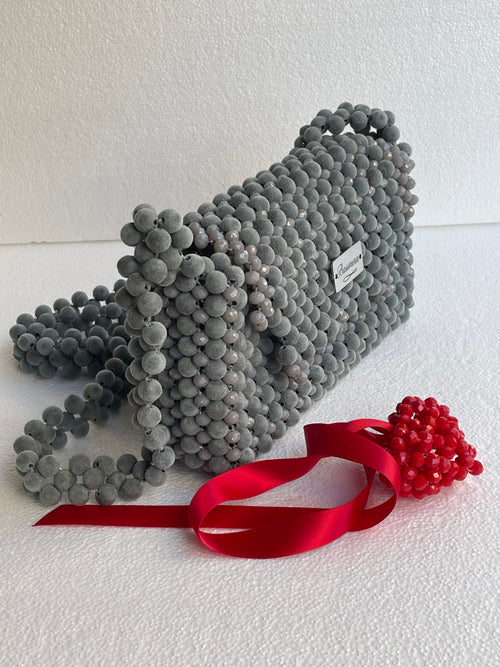 Sac Bassmera Griselle gris en perles associé à un ornement cœur rouge et un ruban de satin, vue de trois quarts.