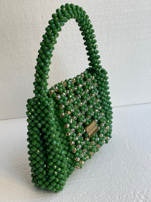 Sac Bassmera Emeraudea artisanal tissé en cristal vert émeraude avec accents champagne, vue de trois quarts latérale avec poignée et plaque dorée.