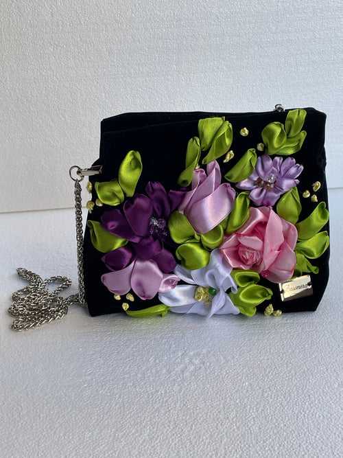 Sac à main Bassmera Florensa en velours noir, vue de face avec fleurs 3D en satin, feuilles vertes et chaîne argentée.