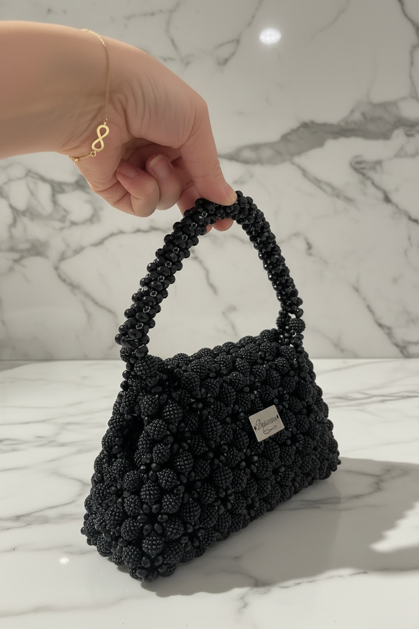 Black Bassmera beaded bag close-up held by hand on marble background